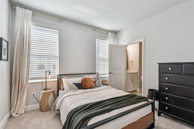 bedroom with light colored carpet, baseboards, and ensuite bath