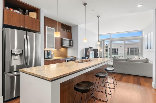 kitchen with a breakfast bar area, dark wood-type flooring, a sink, appliances with stainless steel finishes, and backsplash