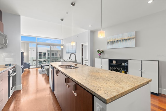 kitchen featuring an island with sink, appliances with stainless steel finishes, light wood-type flooring, pendant lighting, and a sink