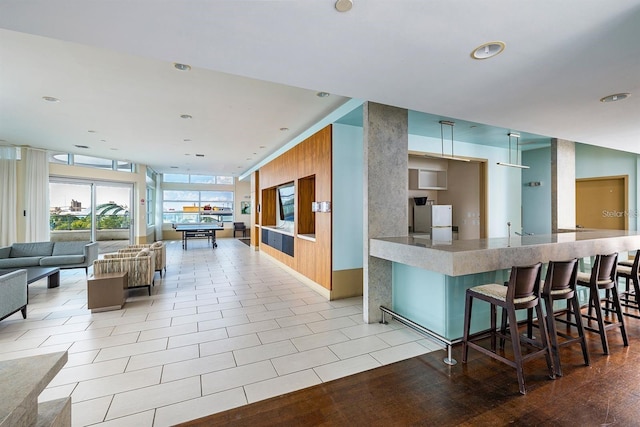 interior space featuring light tile patterned floors, recessed lighting, open floor plan, freestanding refrigerator, and a kitchen bar