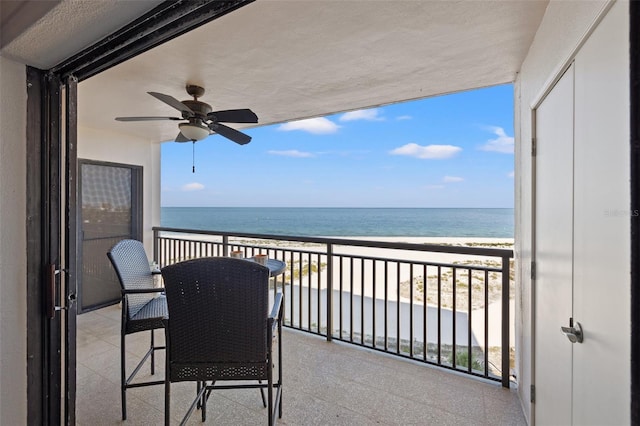 balcony with a water view, a view of the beach, and a ceiling fan