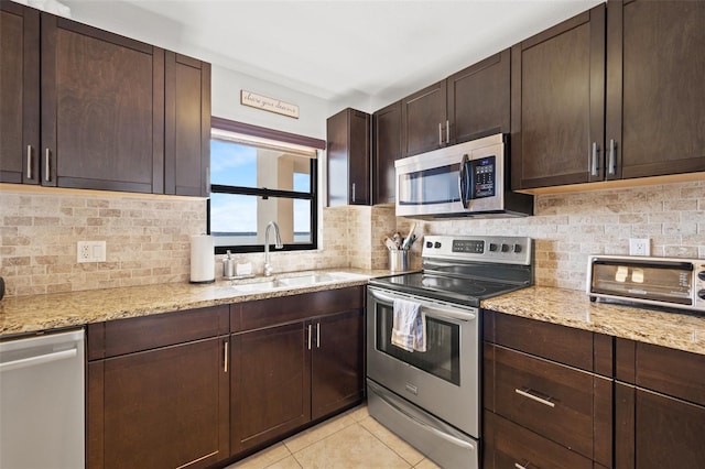 kitchen with light tile patterned floors, dark brown cabinetry, a sink, appliances with stainless steel finishes, and decorative backsplash