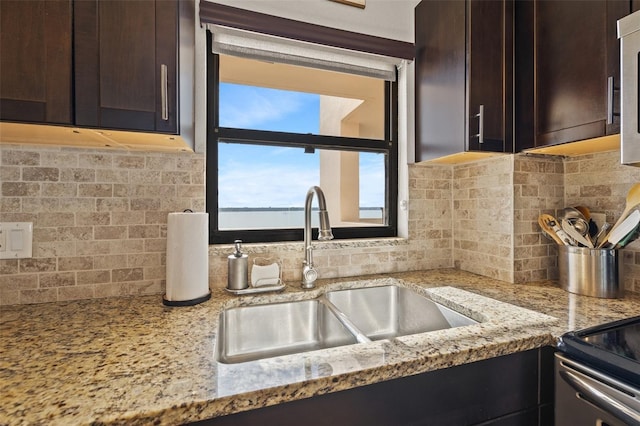 kitchen featuring dark brown cabinets, tasteful backsplash, a sink, and light stone countertops