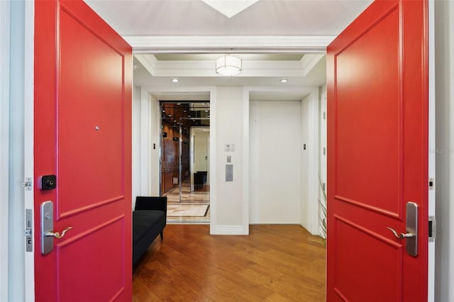 entryway with a raised ceiling, wood finished floors, and ornamental molding