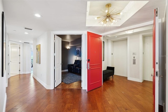 corridor with a notable chandelier, visible vents, baseboards, and hardwood / wood-style flooring