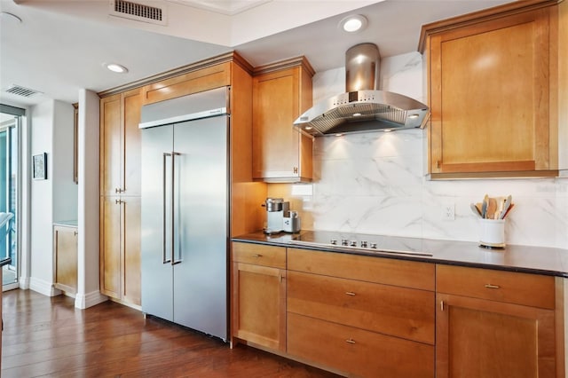 kitchen with black electric cooktop, wall chimney exhaust hood, visible vents, and built in refrigerator