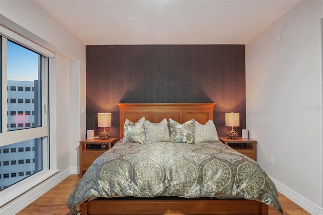 bedroom featuring light wood finished floors, an accent wall, and baseboards