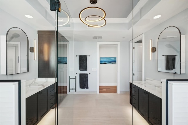 bathroom with visible vents, a raised ceiling, baseboards, and two vanities