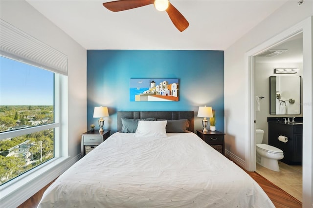 bedroom with visible vents, connected bathroom, baseboards, wood finished floors, and a ceiling fan