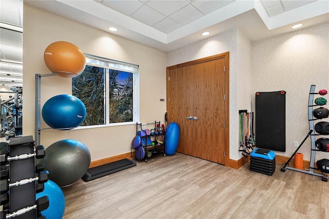 workout room featuring a tray ceiling, recessed lighting, wood finished floors, and baseboards