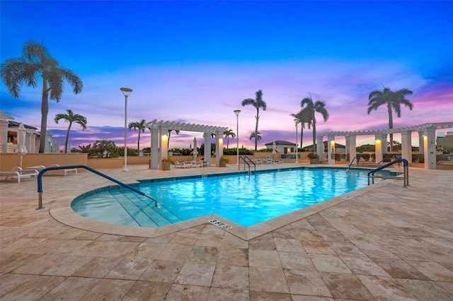 pool at dusk with a community pool, a patio area, and a pergola