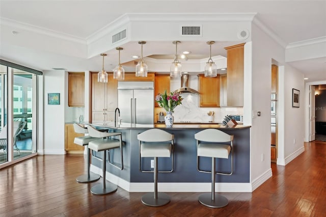 kitchen with built in refrigerator, wall chimney exhaust hood, visible vents, and dark wood-style flooring