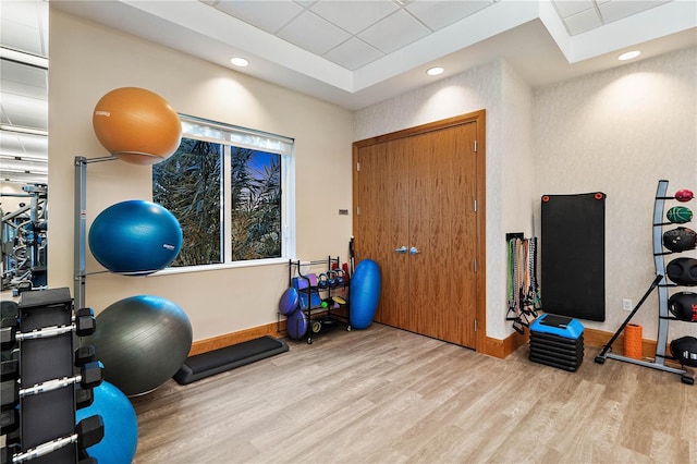 workout area featuring baseboards, a raised ceiling, a drop ceiling, and wood finished floors