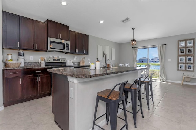 kitchen with light tile patterned floors, stainless steel appliances, visible vents, dark stone counters, and a kitchen breakfast bar