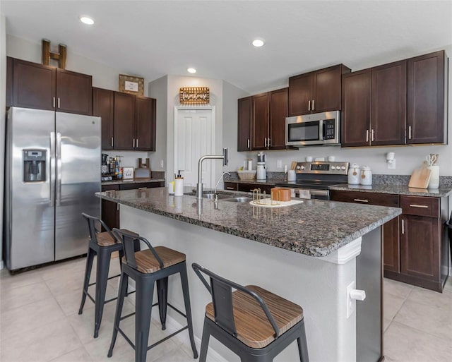 kitchen with a breakfast bar area, recessed lighting, stainless steel appliances, a sink, and dark stone countertops