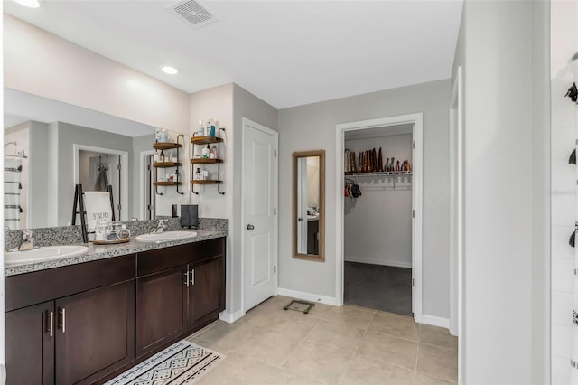 bathroom featuring double vanity, visible vents, a walk in closet, and a sink