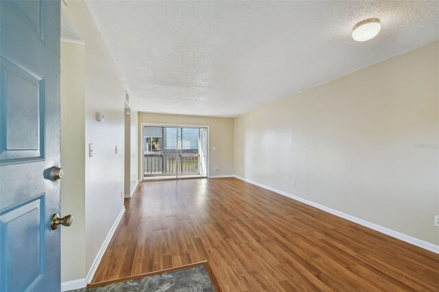 empty room featuring a textured ceiling, baseboards, and wood finished floors