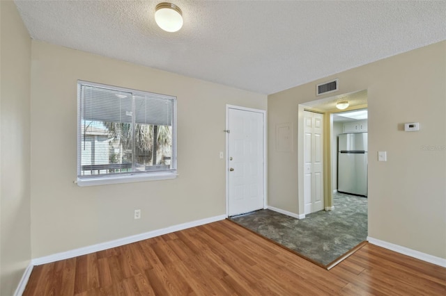 unfurnished room with visible vents, a textured ceiling, baseboards, and wood finished floors