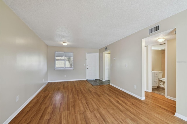 unfurnished living room featuring a textured ceiling, light wood finished floors, visible vents, and baseboards