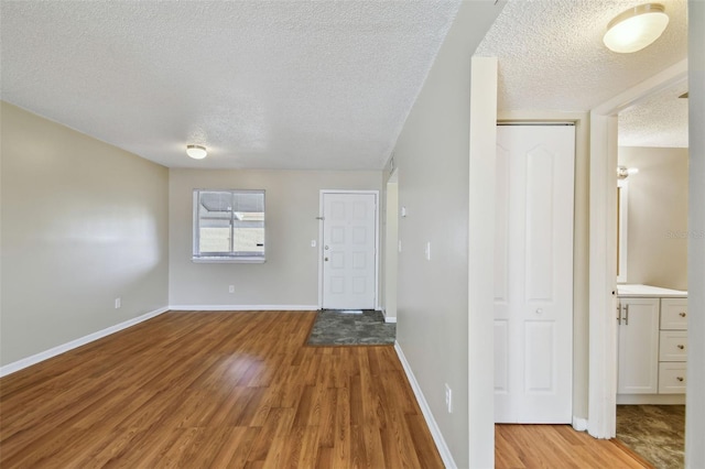 foyer entrance with a textured ceiling, baseboards, and wood finished floors