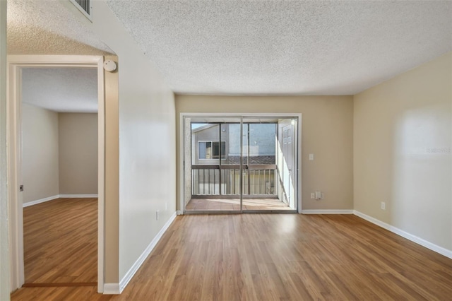unfurnished room with a textured ceiling, wood finished floors, visible vents, and baseboards