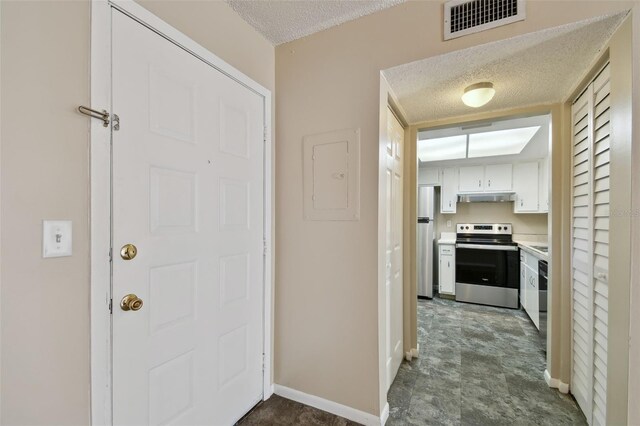 hall featuring a textured ceiling, electric panel, visible vents, and baseboards