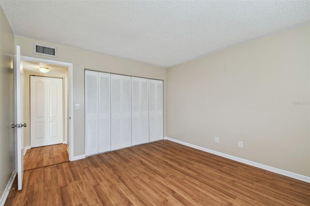 unfurnished bedroom with a textured ceiling, visible vents, baseboards, a closet, and light wood-type flooring
