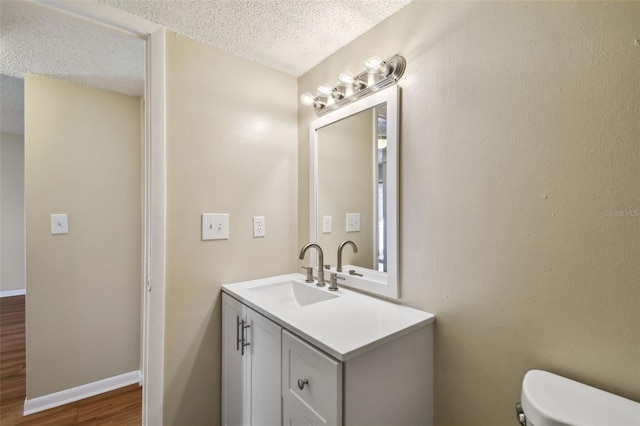 half bathroom with a textured ceiling, toilet, wood finished floors, vanity, and baseboards