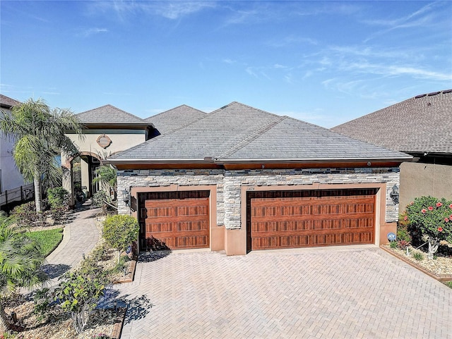 view of front facade featuring stone siding, decorative driveway, and an attached garage