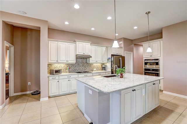 kitchen featuring light tile patterned flooring, a kitchen island with sink, under cabinet range hood, stainless steel appliances, and tasteful backsplash