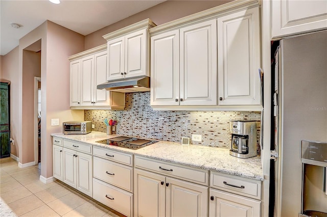 kitchen featuring stainless steel refrigerator with ice dispenser, tasteful backsplash, light tile patterned flooring, under cabinet range hood, and black electric cooktop