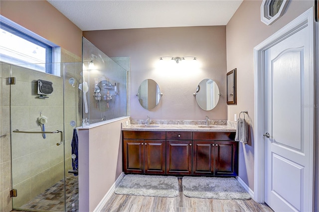 full bathroom with double vanity, wood finished floors, a stall shower, and a sink