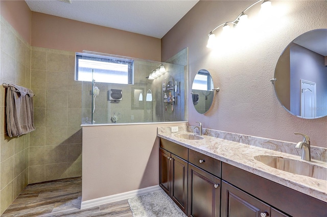 full bathroom featuring double vanity, walk in shower, a sink, and wood finished floors