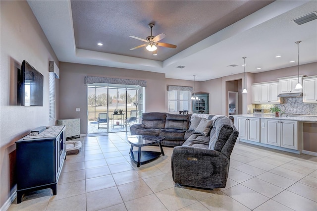 living room featuring light tile patterned floors, a raised ceiling, visible vents, and a ceiling fan
