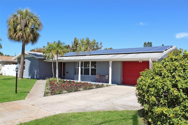 view of front of home with brick siding, solar panels, concrete driveway, an attached garage, and a front yard