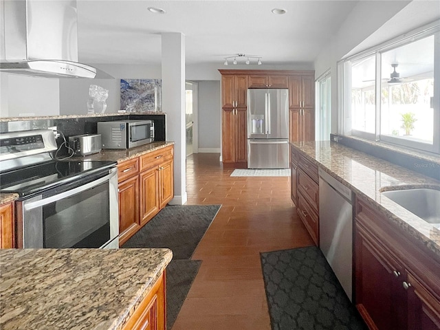 kitchen featuring appliances with stainless steel finishes, brown cabinetry, light stone counters, and extractor fan