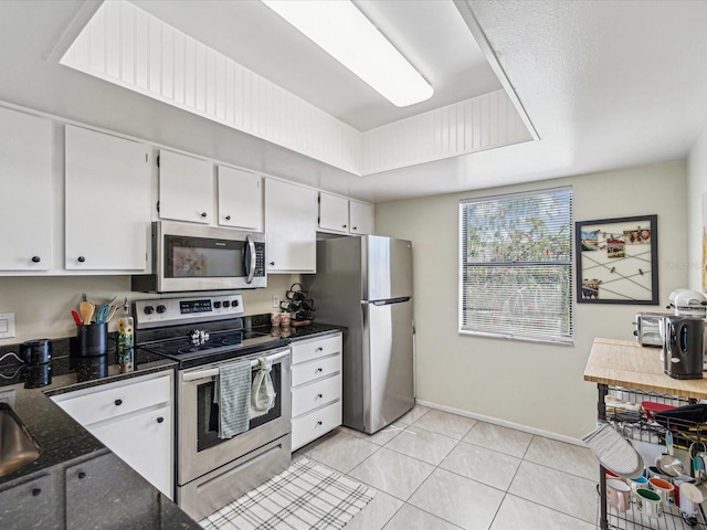 kitchen featuring light tile patterned flooring, baseboards, white cabinets, appliances with stainless steel finishes, and a raised ceiling