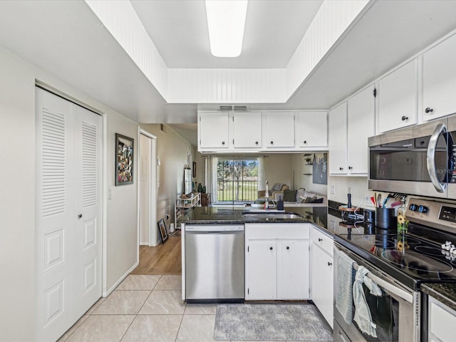 kitchen featuring a tray ceiling, stainless steel appliances, white cabinetry, a sink, and light tile patterned flooring