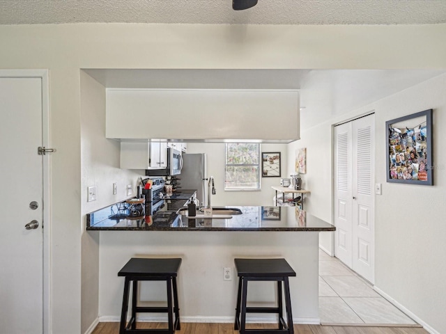 kitchen featuring a kitchen breakfast bar, a peninsula, stainless steel appliances, white cabinetry, and a sink