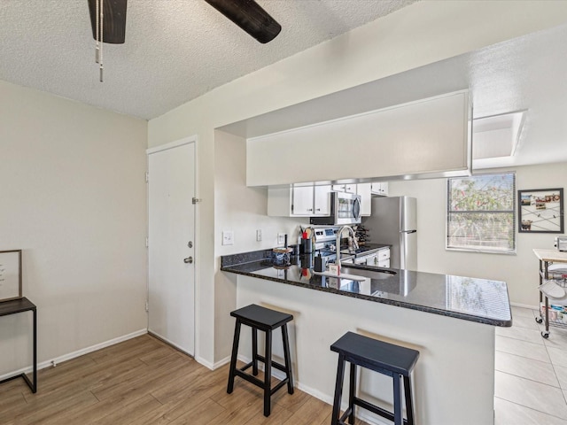 kitchen featuring stainless steel appliances, white cabinetry, a sink, a peninsula, and a kitchen bar