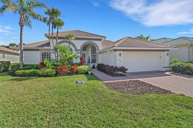 mediterranean / spanish home featuring decorative driveway, stucco siding, an attached garage, a front yard, and a tiled roof