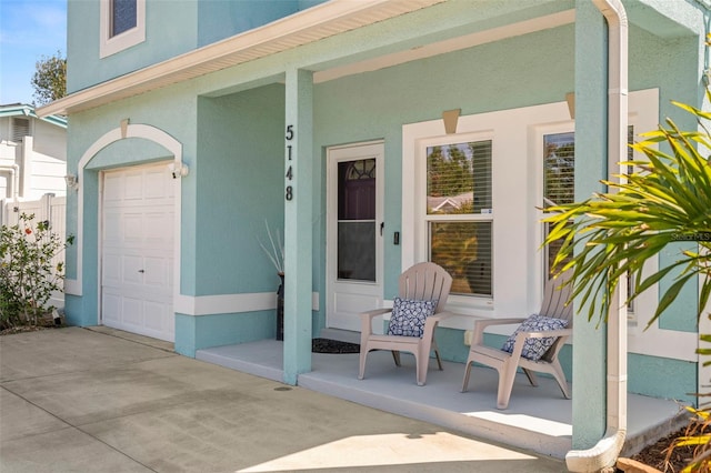 view of exterior entry featuring a garage, covered porch, and stucco siding