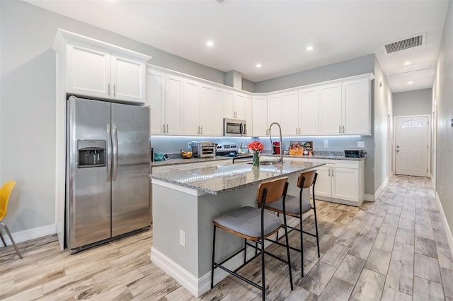 kitchen with a center island with sink, visible vents, white cabinets, light stone countertops, and stainless steel appliances