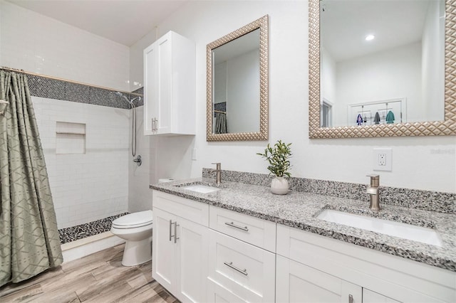 bathroom featuring a sink, a tile shower, toilet, and wood finished floors