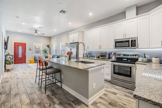 kitchen featuring visible vents, light wood-style flooring, light stone counters, stainless steel appliances, and a sink