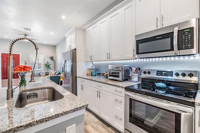 kitchen with stainless steel appliances, a sink, visible vents, white cabinetry, and light wood finished floors