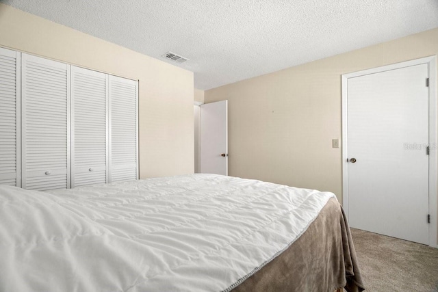 carpeted bedroom with a textured ceiling, a closet, and visible vents