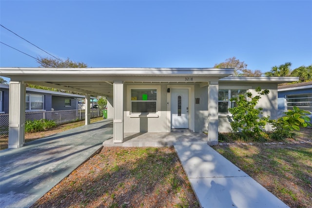 view of front facade featuring an attached carport, covered porch, fence, concrete driveway, and stucco siding