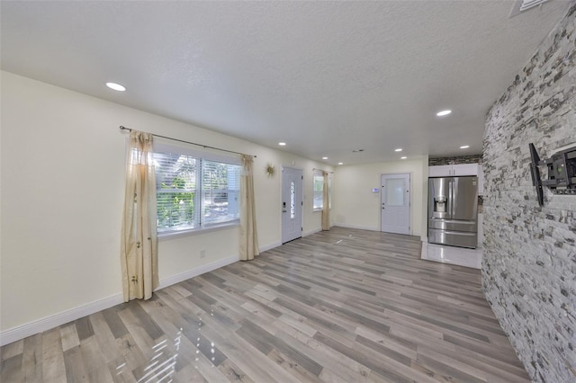 unfurnished living room featuring a textured ceiling, recessed lighting, baseboards, and light wood-style floors