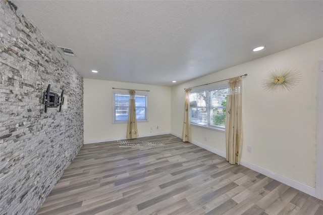 empty room featuring visible vents, a textured ceiling, baseboards, and wood finished floors